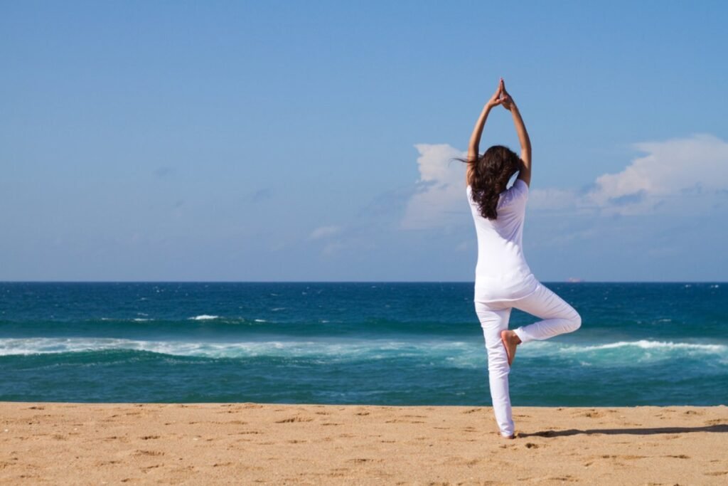 Woman doing yoga on sandy beach by the ocean.