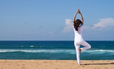 Woman doing yoga on sandy beach by the ocean.