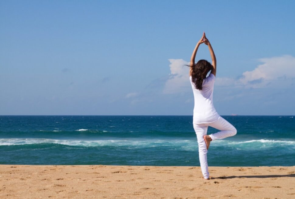 Woman doing yoga on sandy beach by the ocean.