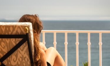 Guest enjoying ocean-view balcony with drink for stress relief